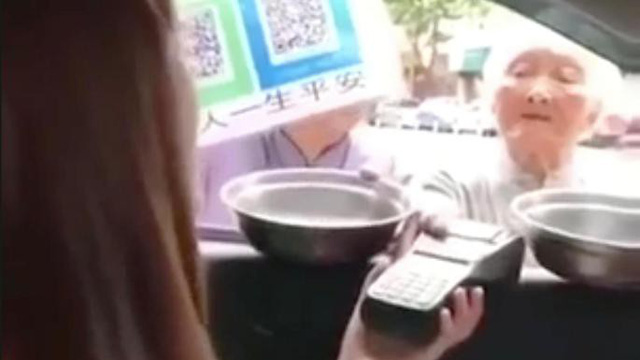 Một bà lão ăn xin người Trung Quốc đang xin tiền bằng máy POS quẹt thẻ ATM. (Nguồn: The Times)