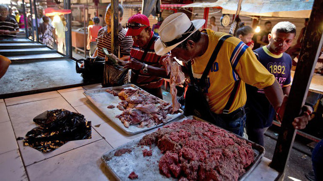 Một khách hàng đang ngửi thử một miếng thịt thối tại một chợ ở thành phố Maracaibo, Venezuela. (Nguồn: Chicago Tribune)