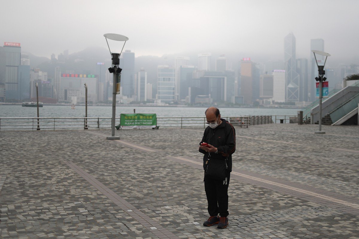 A man wearing a face mask checks his phone in a deserted Tsim Sha Tsui. The waterfront is normally bustling with tourists to the city. Photo: Winson Wong