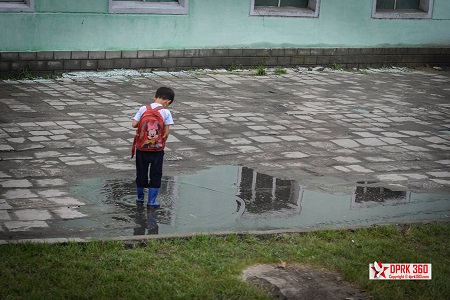 Một cậu bé tha thẩn chơi bên vũng nước mưa trên đường đi học về.