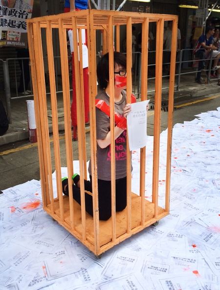 Một người biểu tình quỳ trong lồng, phản đối sách trắng của Trung Quốc