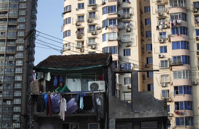 Một phụ nữ đứng trên ban công căn nhà lẽ ra đã được giải tỏa để nhường chỗ cho một dự án chung cư ở Thượng Hải hôm 1/12/2010 - Ảnh: Reuters.